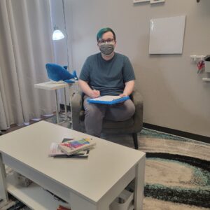 Masked person seated in chair writing on clipboard